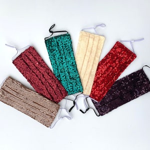 May include: Six face masks made of sparkly fabric. The masks are in various colors, including gold, red, purple, teal, and cream.