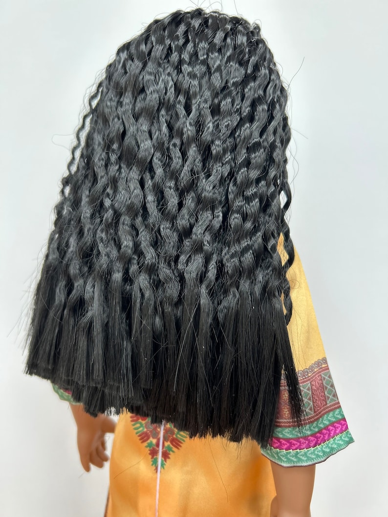 Puede incluir: Una mu&ntilde;eca con pelo largo, negro y rizado. La mu&ntilde;eca lleva un vestido amarillo con un dise&ntilde;o estampado colorido en las mangas y el dobladillo. El pelo est&aacute; peinado de forma voluminosa y texturizada.