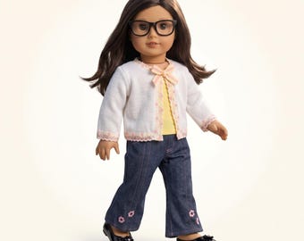 May include: A doll with long brown hair and black-rimmed glasses, wearing a white knit cardigan with a small bow, a yellow shirt, dark blue denim flared pants with small pink flower embroidery at the hems, and black flat shoes.