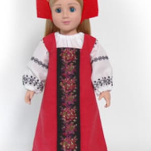 May include: A doll with blonde hair wearing a red kokoshnik headpiece with gold trim. The doll is dressed in a white long-sleeved blouse with black embroidery on the sleeves and a red pinafore dress featuring a central black panel with floral embroidery.