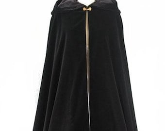 May include: A floor-length black velvet cloak featuring a hood and a gold-toned metal clasp at the neckline. The garment has a smooth, dark fabric texture and hangs in vertical folds, with a visible inner lining visible at the hood opening.