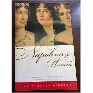 May include: A book cover featuring portraits of three women with the title "Napoleon's Women" in gold script. The author's name, Christopher Hibbert, is printed in white on a red band at the bottom. A quote from Kirkus Reviews is also included.