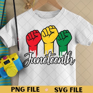 May include: White t-shirt featuring three raised fists in red, yellow, and green, with the word "Juneteenth" in a script font. A blue and yellow toy camera hangs in the foreground.