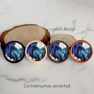 May include: Four round decorative knobs with a dragon design in shades of blue, purple, and white. The knobs have different colored frames: black, light wood, dark wood, and reddish-brown. The text "---johill design" is visible.
