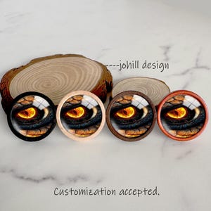 May include: Four round decorative objects featuring a close-up of a dragon's eye with a yellow iris and black, blue, and brown details. The objects are set on a wooden surface. Text reads "---johill design" and "Customization accepted."