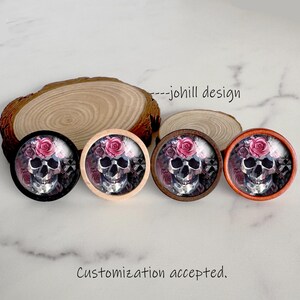 May include: Four decorative skull designs with rose accents. Each skull has a different colored border: black, natural wood, brown, and orange. The text "---johill design" is visible.