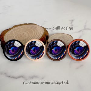 May include: Four round decorative buttons featuring a close-up of a dragon's eye in shades of blue, purple, and yellow. The buttons have different colored frames: black, natural wood, dark brown, and orange. The text "---johill design" and "Customization accepted" are visible.