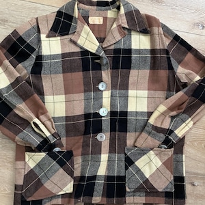 May include: A vintage plaid jacket in shades of brown, black, and cream. The jacket features a collared neckline, button-up front, two front pockets, and long sleeves. The fabric has a classic plaid pattern.