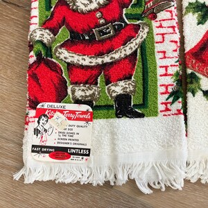 K&ouml;nnte beinhalten: Vintage Weihnachts-K&uuml;chent&uuml;cher mit einem Weihnachtsmann-Design. Die Handt&uuml;cher sind wei&szlig; mit einem Fransenrand und zeigen eine rot-gr&uuml;ne Weihnachtsmann-Illustration. Die Handt&uuml;cher haben ein Etikett mit der Aufschrift "Deluxe Kitchen Terry Towels".