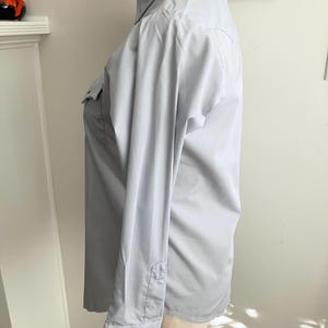 May include: A light blue long-sleeved button-down shirt with a pointed collar and two chest pockets.