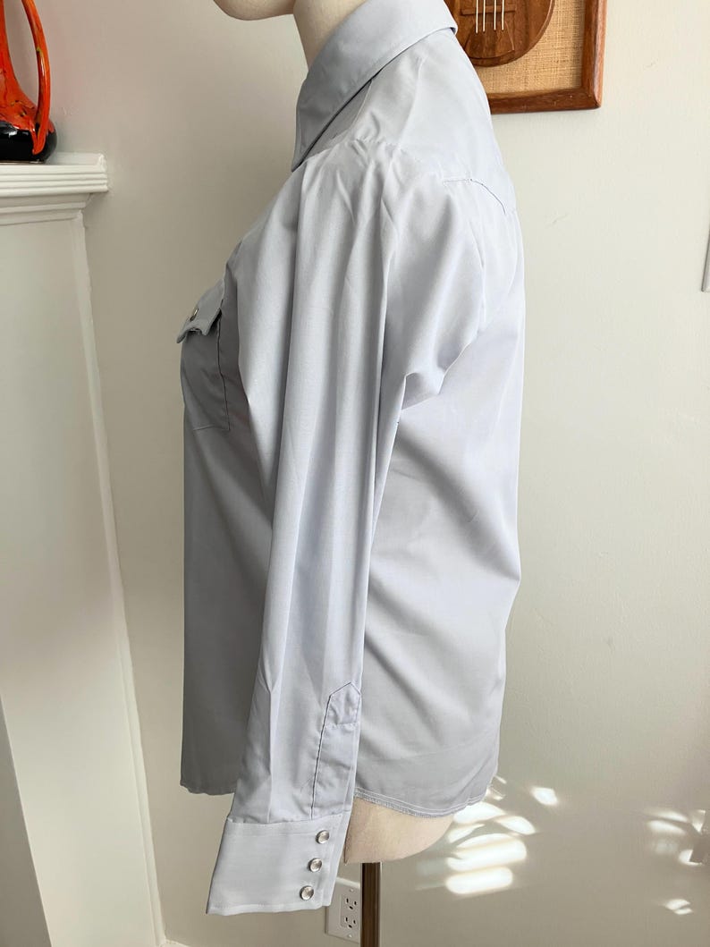 May include: A light blue long-sleeved button-down shirt with a pointed collar and two chest pockets.