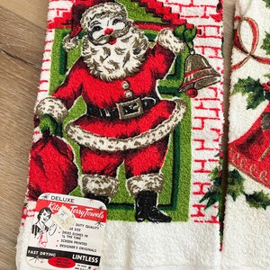 K&ouml;nnte beinhalten: Vintage Weihnachts-K&uuml;chent&uuml;cher mit einem rot-wei&szlig;en Weihnachtsmann-Design. Die Handt&uuml;cher haben einen wei&szlig;en Fransen und ein Etikett mit der Aufschrift "Deluxe Kitchen Terry Towels". Die Weihnachtsmann-Illustration umfasst einen roten Anzug, einen wei&szlig;en Bart und eine Glocke.