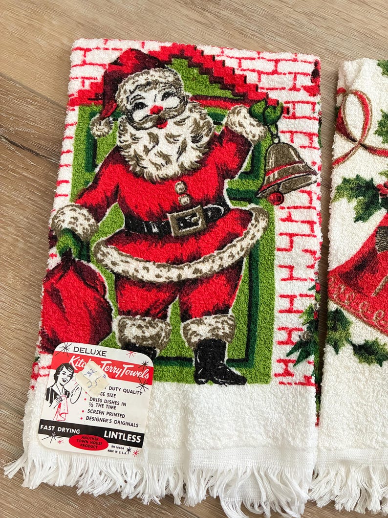 K&ouml;nnte beinhalten: Vintage Weihnachts-K&uuml;chent&uuml;cher mit einem rot-wei&szlig;en Weihnachtsmann-Design. Die Handt&uuml;cher haben einen wei&szlig;en Fransen und ein Etikett mit der Aufschrift "Deluxe Kitchen Terry Towels". Die Weihnachtsmann-Illustration umfasst einen roten Anzug, einen wei&szlig;en Bart und eine Glocke.