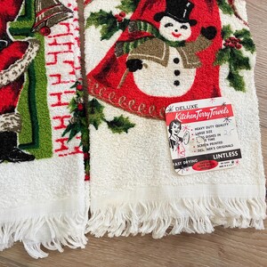 K&ouml;nnte beinhalten: Zwei Vintage-Weihnachts-K&uuml;chent&uuml;cher. Eines zeigt den Weihnachtsmann in einem roten Anzug, das andere einen Schneemann mit Zylinder. Beide haben wei&szlig;e Fransen und den Text "DELUXE Kitchen Terry Towels".