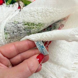K&ouml;nnte beinhalten: Wei&szlig;es Baumwolltuch mit Fransen und einem festlichen Weihnachtsdesign in Rot, Gr&uuml;n und Wei&szlig;. Das Handtuch hat ein Etikett mit der Aufschrift "CANNON ALL COTTON MADE IN USA".