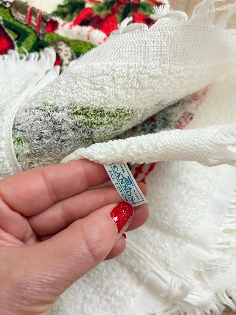 K&ouml;nnte beinhalten: Wei&szlig;es Baumwolltuch mit Fransen und einem festlichen Weihnachtsdesign in Rot, Gr&uuml;n und Wei&szlig;. Das Handtuch hat ein Etikett mit der Aufschrift "CANNON ALL COTTON MADE IN USA".