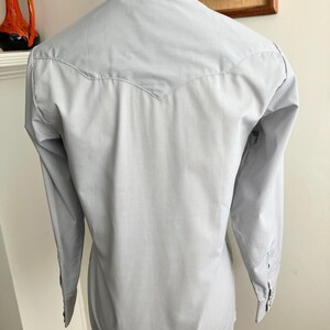 May include: A light blue long-sleeved shirt with a pointed yoke at the back.