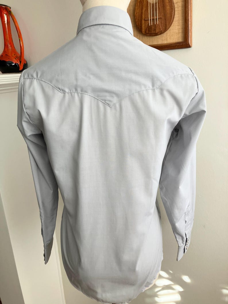 May include: A light blue long-sleeved shirt with a pointed yoke at the back.
