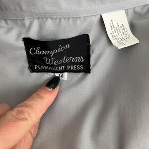 May include: A grey long-sleeved shirt with a black label that reads "Champion Westerns Permanent Press" and a size tag that reads "4".