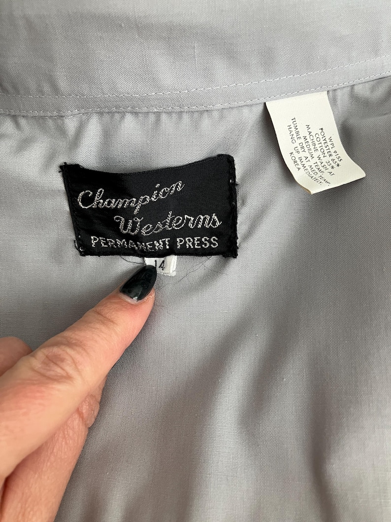 May include: A grey long-sleeved shirt with a black label that reads "Champion Westerns Permanent Press" and a size tag that reads "4".