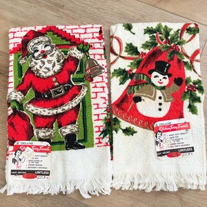K&ouml;nnte beinhalten: Zwei Vintage-Weihnachts-K&uuml;chent&uuml;cher. Eines zeigt den Weihnachtsmann mit Glocke und Sack, das andere einen Schneemann mit Stechpalme. Beide haben wei&szlig;e Fransen und Etiketten mit der Aufschrift "Deluxe Kitchen Terry Towels".