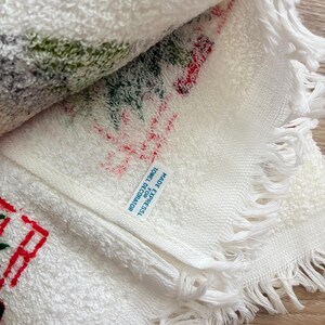 K&ouml;nnte beinhalten: Wei&szlig;es dekoratives Handtuch mit roten und gr&uuml;nen Stickereidetails. Das Handtuch hat einen Fransenrand und den Text "MADE FOR EXPRESSL TOWEL DECORATOR". Das Handtuch ist gefaltet und zeigt das gestickte Design.