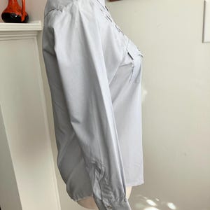 May include: A light blue long-sleeved button-up shirt with a pointed collar and a single chest pocket.
