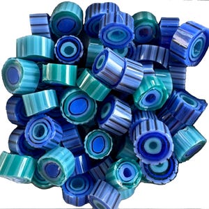 May include: A collection of blue and teal glass beads. The beads are cylindrical with striped and concentric circle patterns. The color palette includes shades of blue, teal, and white. The beads are likely for jewelry making or other craft projects.