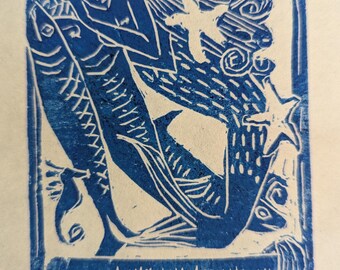 May include: Blue and white linocut print of a mermaid with flowing hair holding a fish. The mermaid is surrounded by waves and a starfish.
