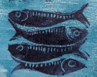 May include: A close-up of a blue textile featuring a pattern of stylized fish in dark blue. The fish are stacked, with details including fins, eyes, and scale patterns. The background is a lighter blue with a textured appearance.