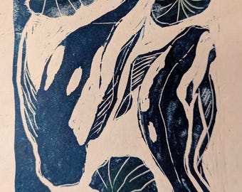 May include: A blue and white linocut print featuring two koi fish swimming among lily pads. The fish are a deep blue, with white details. The lily pads are green, and the background is off-white.