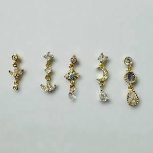 May include: Five gold-toned earrings with various designs, including stars, moons, and teardrops, each adorned with clear and blue gemstones. The earrings are displayed against a plain white background.