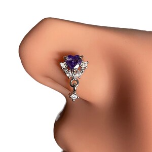May include: A silver nose ring with a dangling charm. The charm features a purple heart-shaped stone surrounded by smaller clear stones.