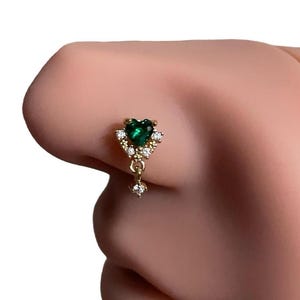 May include: A gold nose ring with a green heart-shaped gemstone and a dangling chain of smaller clear gemstones.