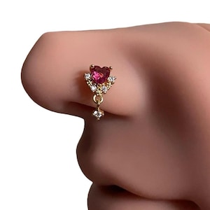 May include: A gold nose ring with a dangling heart-shaped pink gemstone surrounded by clear rhinestones.