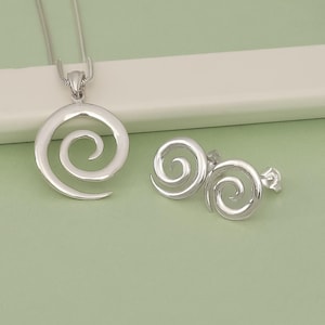 May include: A silver necklace and earrings set featuring a spiral design. The necklace has a chain and a pendant with a single spiral. The earrings have two spirals each.