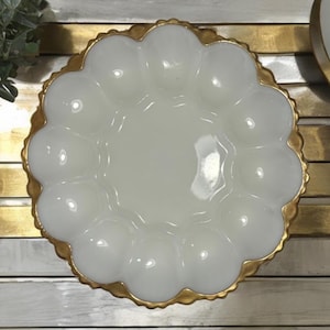 May include: A white glass serving dish with a gold rim. The dish has a scalloped edge and a central well surrounded by twelve rounded compartments. The gold rim adds a touch of elegance to the vintage-style serving piece.