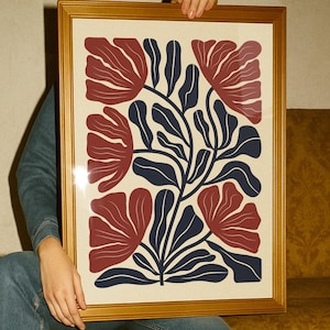 Peut inclure: Impression d'art encadrée avec un motif floral. L'œuvre présente des fleurs rouges stylisées et des feuilles bleu marine sur un fond crème. L'impression est dans un cadre doré, ajoutant une touche d'élégance. Le cadre mesure environ 50 cm x 70 cm.