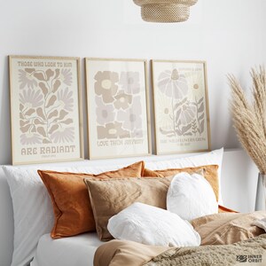May include: Three framed floral art prints with inspirational quotes in neutral tones. The prints feature beige, brown, and white flowers. The text on the prints includes "Those Who Look to Him Are Radiant", "Love Them Anyway", and "The Wildflowers Grow".
