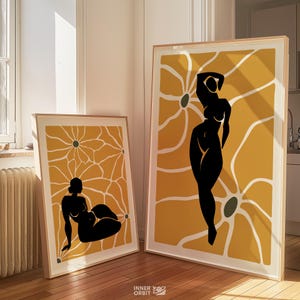 May include: Two framed art prints featuring black silhouettes of figures against a yellow floral background. The prints are in wooden frames and lean against a wall. The art has a modern, minimalist style.