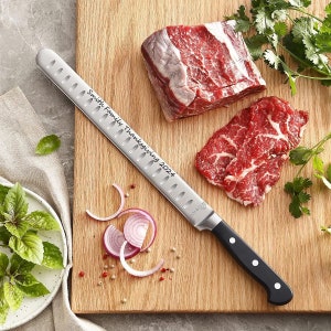 May include: A carving knife with the text "Smith Family Thanksgiving 2024" is placed on a wooden cutting board next to raw beef and fresh herbs. Sliced red onions and peppercorns are also on the board, ready for food preparation.