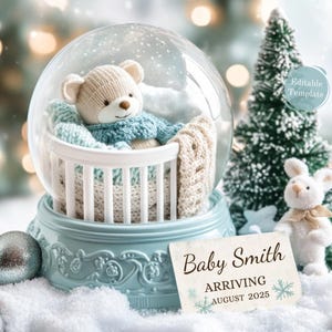 May include: A blue snow globe with a white crib inside. A knitted teddy bear is lying in the crib. A white bunny with a brown ribbon is sitting on a snowy surface next to the snow globe. A white card with the text "Baby Smith Arriving August 2025" is in front of the snow globe.