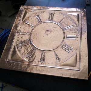 May include: A copper clock face with Roman numeral markings. The face is square and has a hammered texture.