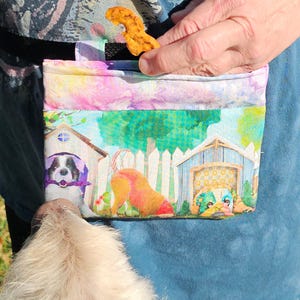 以下が含まれることがあります： 犬のおやつ入れ。犬小屋のプリントが施されたカラフルなポーチ。人が持ち、犬のおやつが見える。犬と犬小屋の水彩画デザインが特徴です。犬のおやつを持ち運ぶように設計されています。