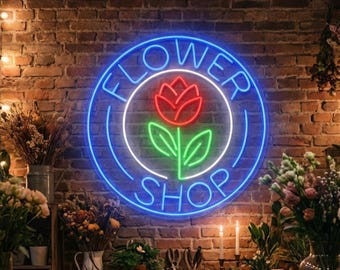 May include: A neon sign for a flower shop, with the words "Flower Shop" encircling a red rose and green leaves. The sign is against a brick wall, with bouquets of flowers and candles on display.