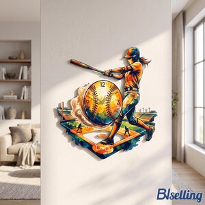 May include: A wall clock featuring a colorful watercolor-style illustration of a baseball player swinging a bat at home plate. The clock face is designed as a baseball with black numbers and hands, set against a vibrant stadium background.