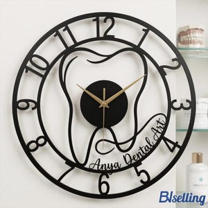 May include: Black metal wall clock with a dental theme. The clock features a tooth design in the center, gold-colored hands, and the words "Anya Dental Art". The clock has a circular frame with numbers.