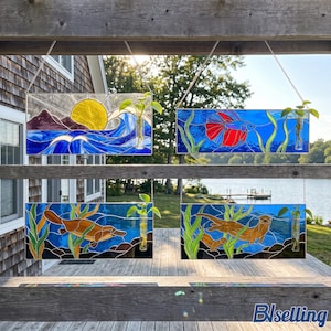 May include: Four rectangular stained glass wall hangings featuring aquatic scenes with a yellow sun over waves, a red betta fish, a brown platypus, and a brown otter, each including a small glass tube for a plant cutting.