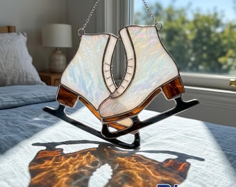 May include: A stained glass suncatcher shaped like a pair of ice skates with iridescent white glass panels, brown accents at the base, and black metal blades. The skates are suspended by a silver chain and cast a warm, orange-toned shadow.