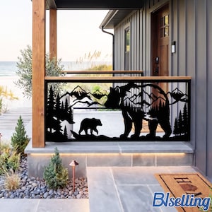 May include: A black metal railing panel featuring a laser-cut silhouette of a large bear and a small bear walking through a forest of pine trees with a mountain range in the background, installed on a porch with wooden posts and a stone floor.